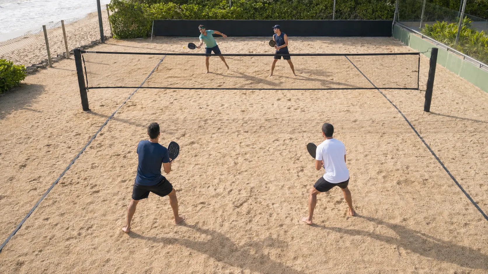 Cancha de beach tennis vista desde una posición elevada detrás de la línea de fondo durante un punto