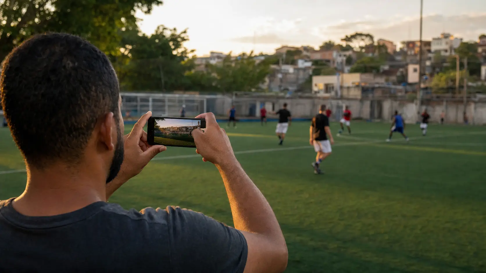Persona filmando un partido de fútbol amateur con el celular desde la línea lateral