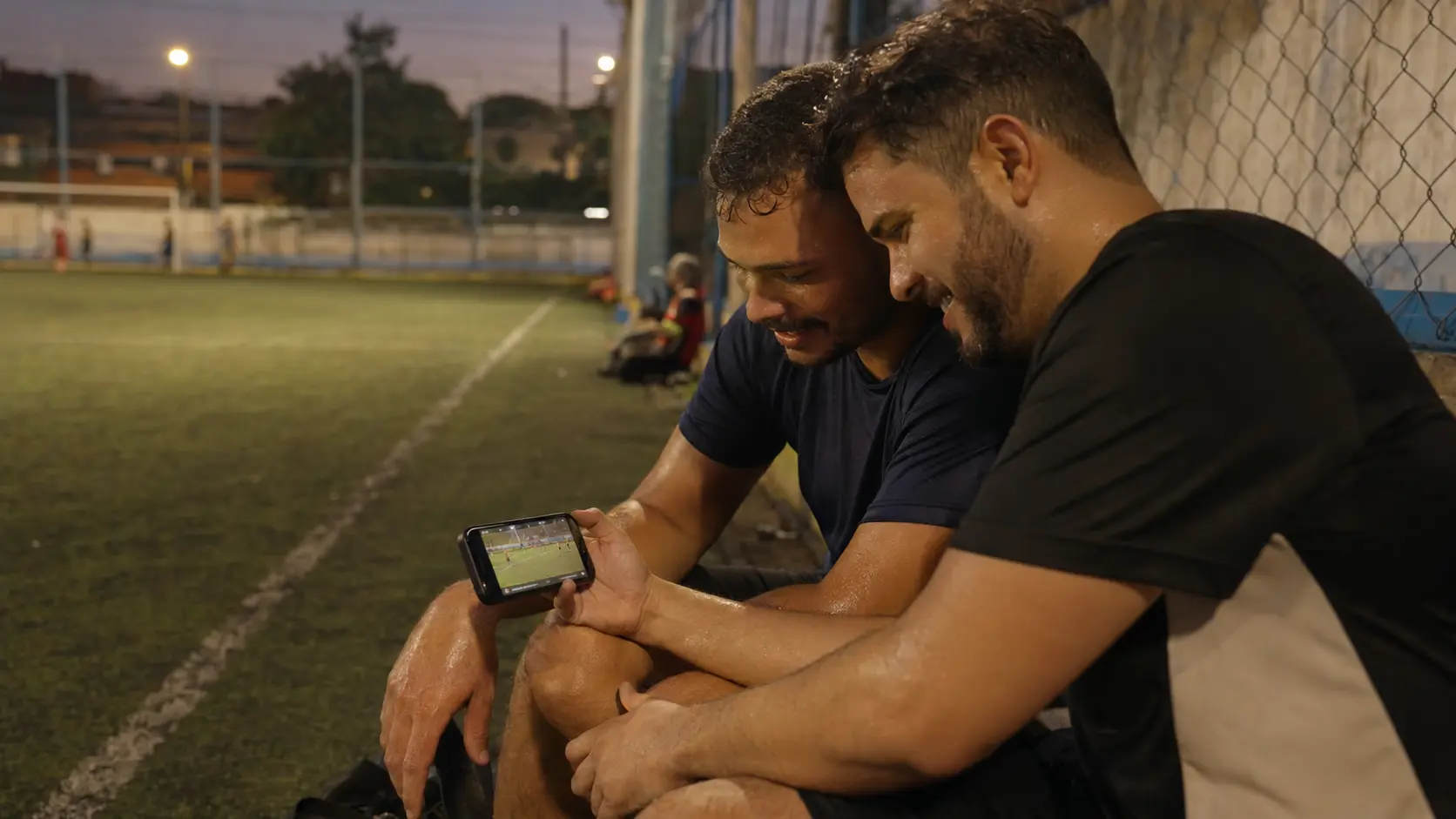 Dos jugadores amateurs sentados al borde de la cancha después de un partido mirando juntos un clip en un celular