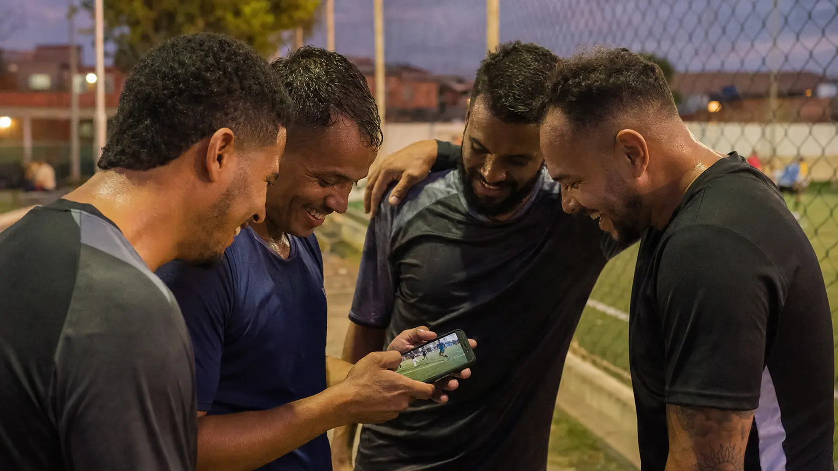 Cuatro jugadores de fútbol amateur amontonados alrededor de un celular después del partido, riéndose