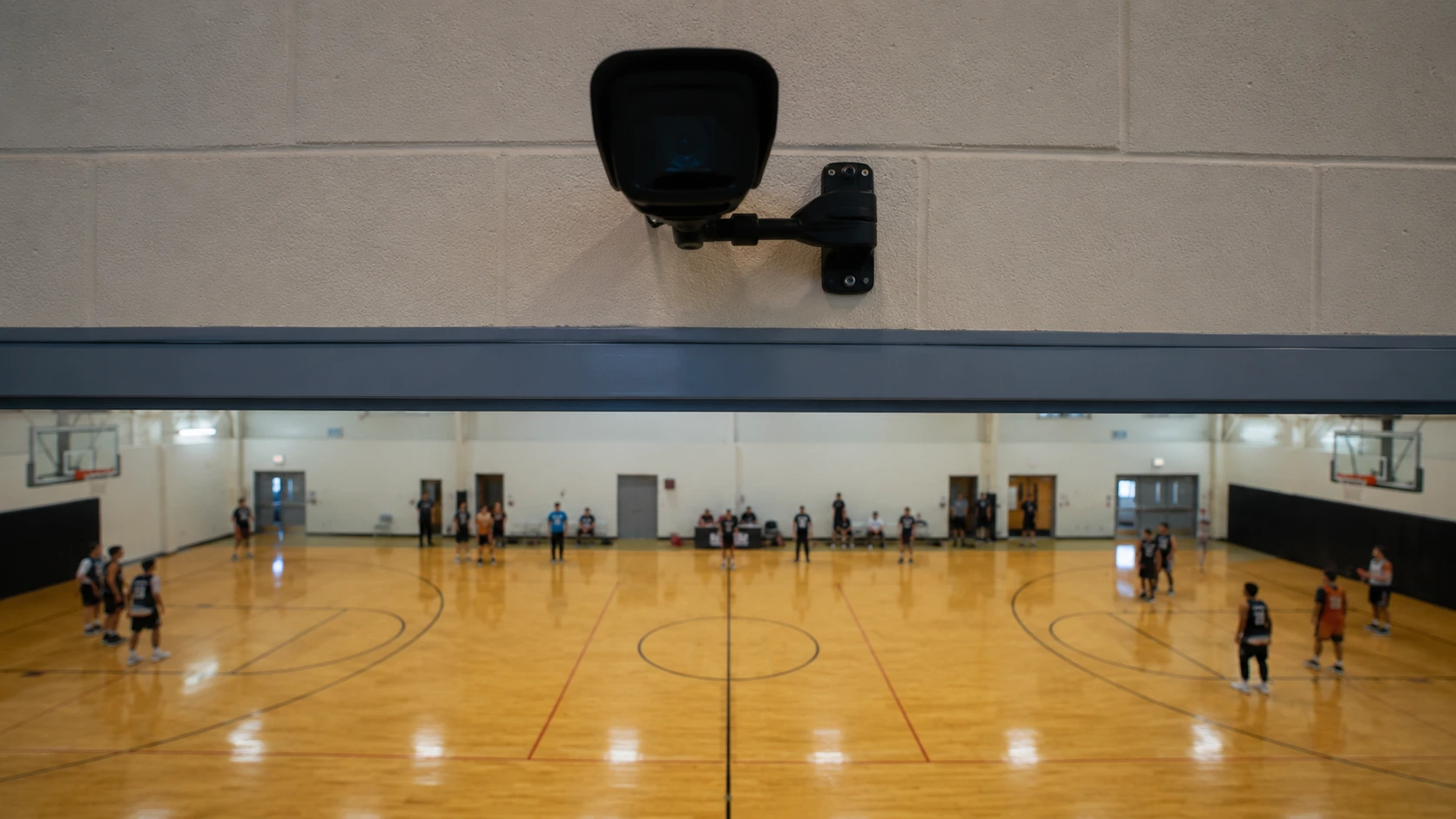 Cámara fija montada sobre el lateral a mitad de cancha en un gimnasio techado con los dos aros de básquetbol a la vista