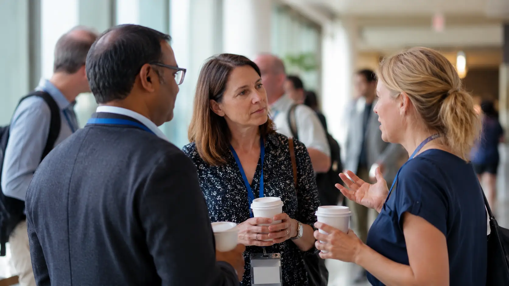 Participantes conversando entre as sessões de um evento corporativo com crachás e café