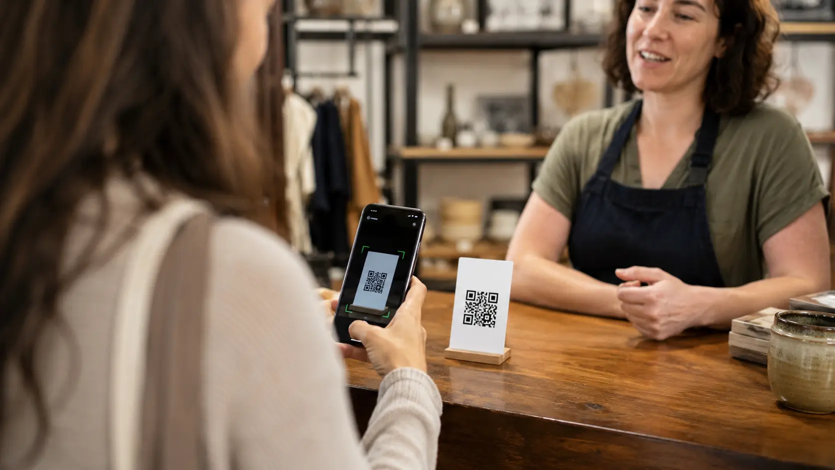 Customer scanning a QR code with a phone at a shop counter while the owner watches