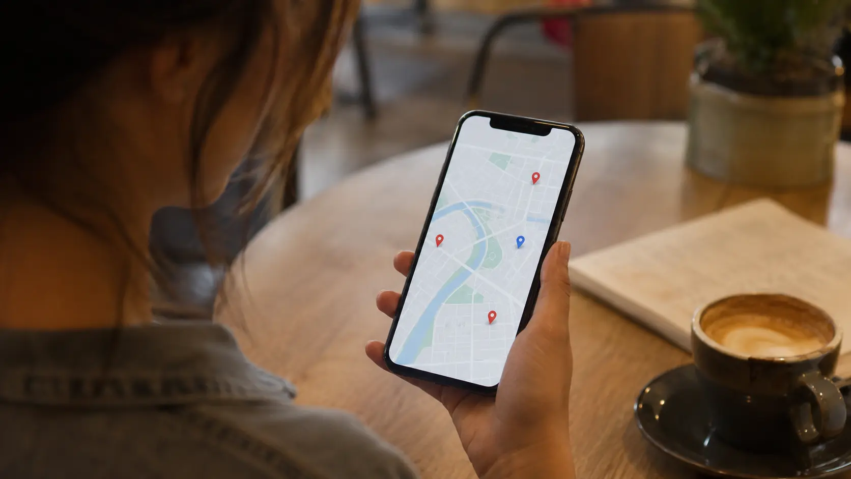 A person at a restaurant table checking a phone showing a map with nearby restaurant listings