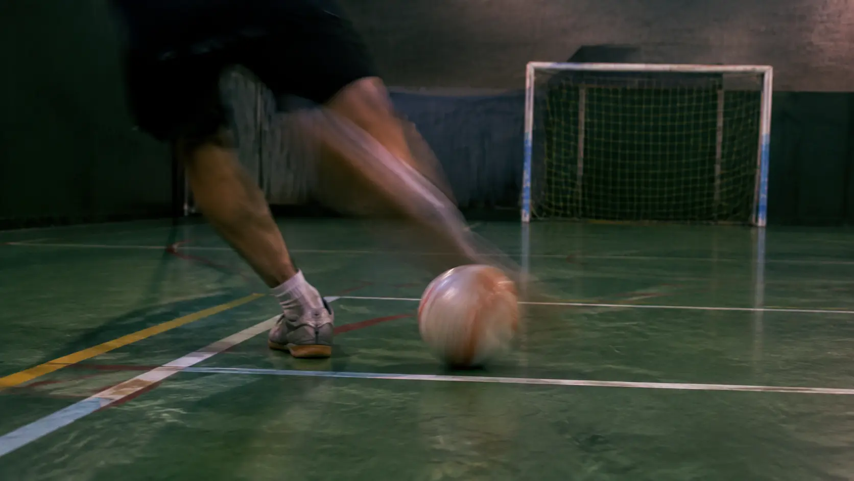 Pelota y pierna de jugador borrosas por el movimiento en una cancha techada mientras el fondo sigue nítido