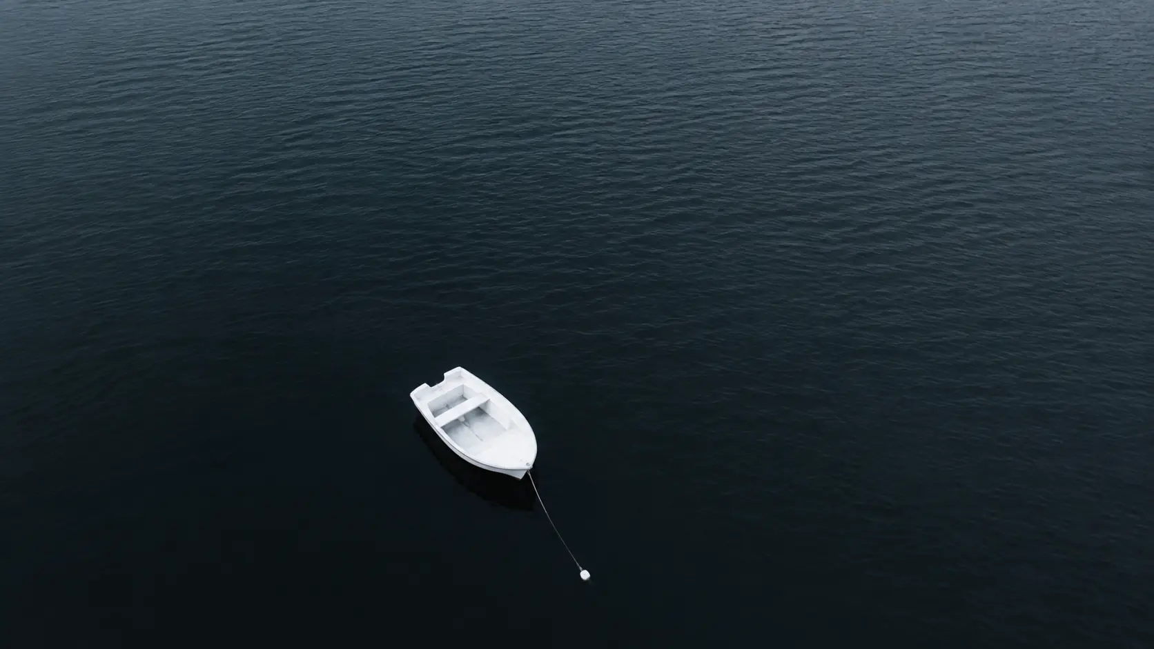 A lone white boat moored on still dark water that fills the entire frame, the boat small and placed low off-center with no shoreline visible