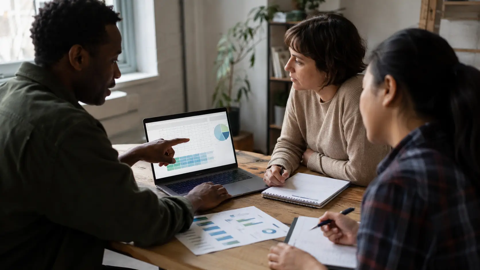 Small nonprofit team around a table reviewing donor data on a laptop and printed reports