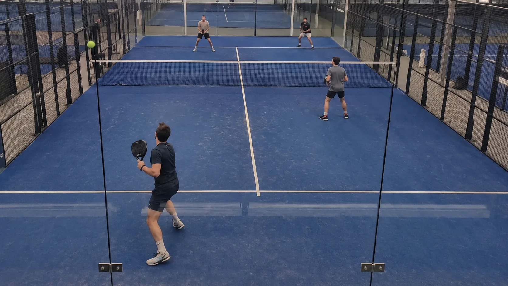 Padel player turned towards the back glass waiting for the ball to rebound, weight moving backwards away from the net