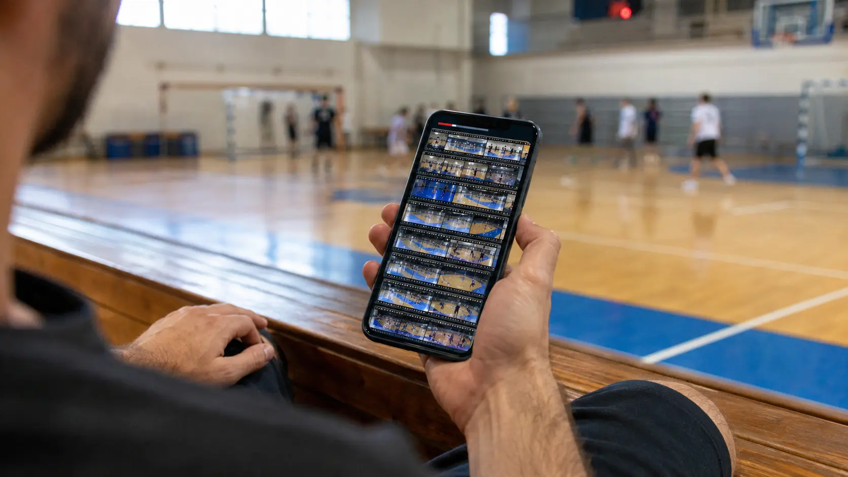 Jugador sentado en la banca de la cancha mirando la pantalla de almacenamiento del celular llena de videos de partidos