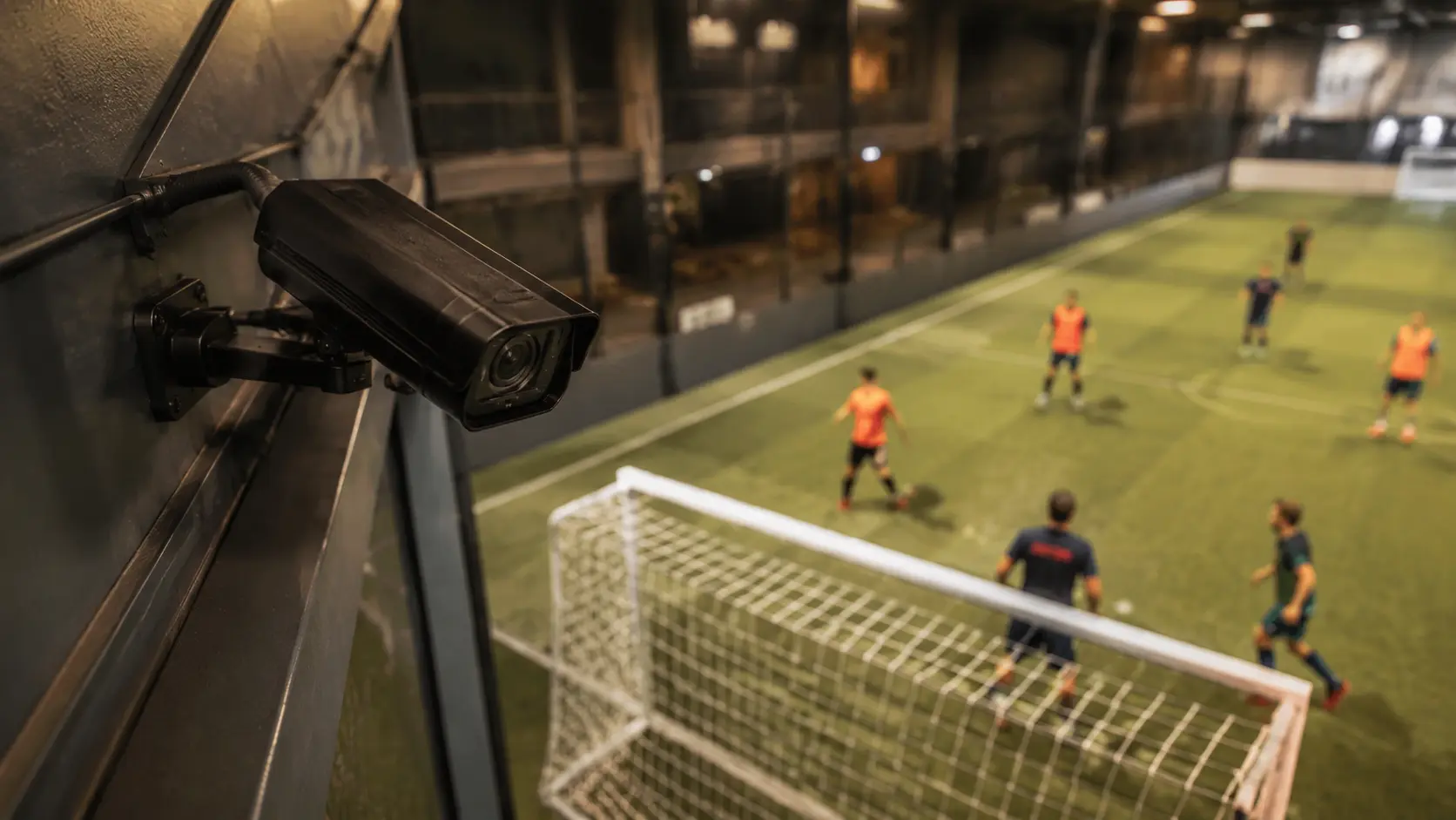 Compact fixed camera mounted high on the wall behind a five-a-side goal during a match