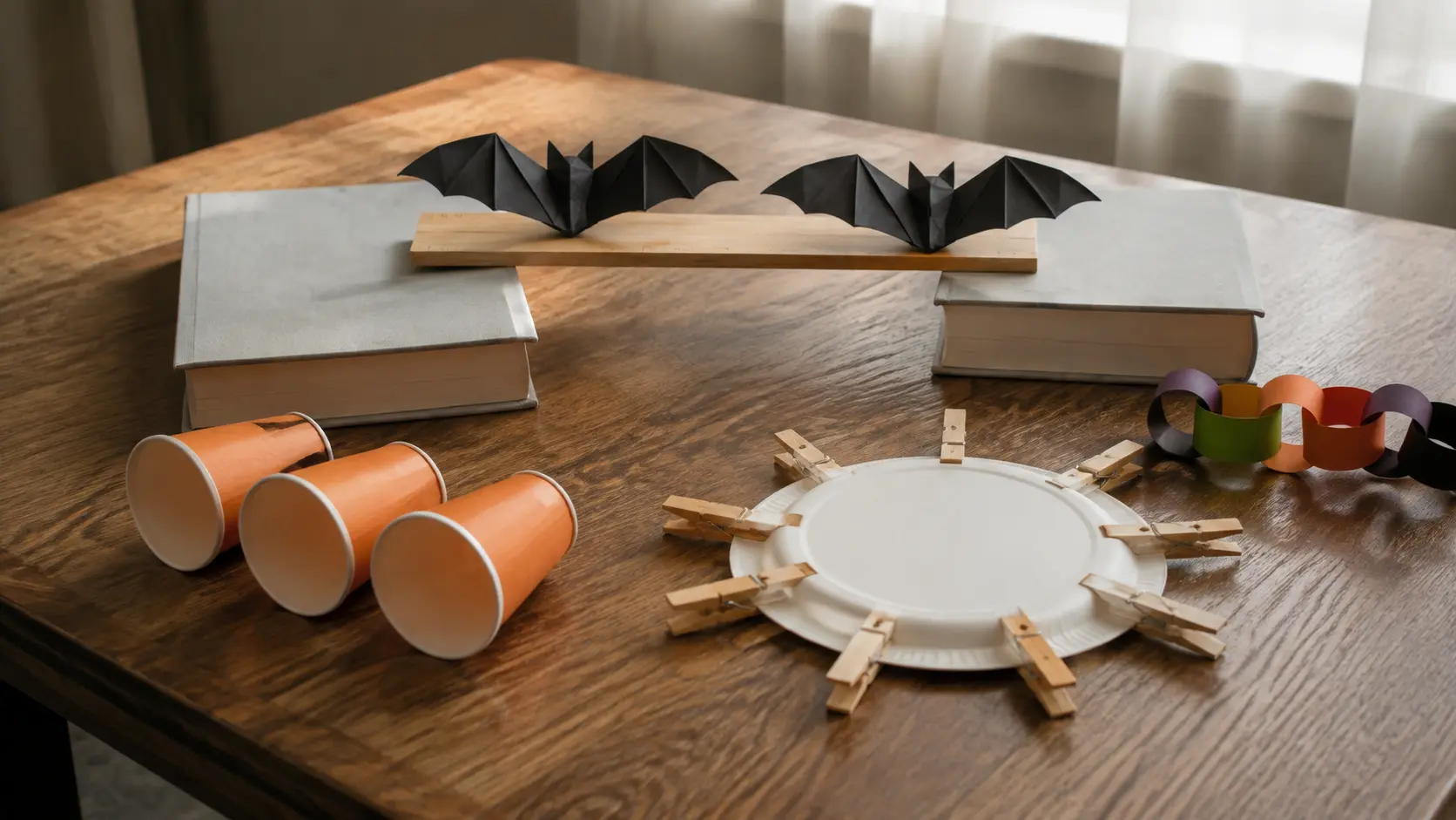 Mesa de desafíos de Halloween con vasos de papel naranja, un plato de papel rodeado de pinzas de ropa, murciélagos de papel doblado sobre una regla y un temporizador de cocina